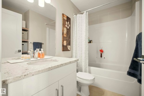 Bathroom featuring a white vanity with an integrated sink, a light-toned countertop, a large wall-mounted mirror, and a built-in bathtub with a shower - 4013 Blackbird Link Nw, Edmonton, AB - Indoor Photo Showing Bathroom