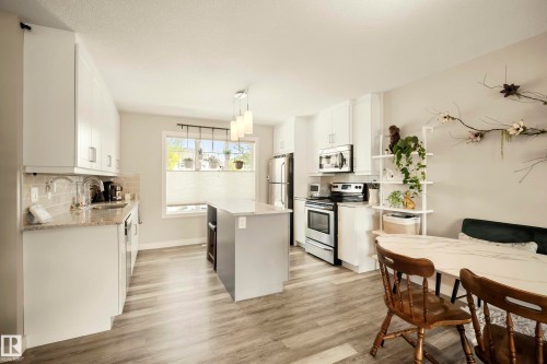 Well-appointed kitchen featuring light-toned cabinetry, stainless steel appliances, a center island with pendant lighting, wood-finish flooring, and a tiled backsplash - 4013 Blackbird Link Nw, Edmonton, AB - Indoor