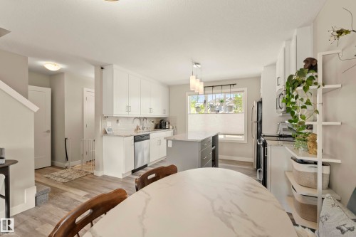 Kitchen featuring white cabinetry, a central island with a contrasting base, stainless steel appliances, and wood-finish flooring - 4013 Blackbird Link Nw, Edmonton, AB - Indoor