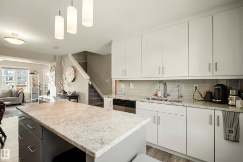 Kitchen featuring white cabinetry, light-toned countertops, a stainless steel sink, and a gray subway tile backsplash - 4013 Blackbird Link Nw, Edmonton, AB - Indoor Photo Showing Kitchen With Double Sink