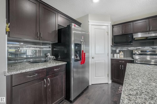 Dark wood-finish cabinetry with silver hardware, speckled countertops, stainless steel appliances, a tile backsplash, and wood-finish flooring - 3359 13 Avenue Nw, Edmonton, AB 