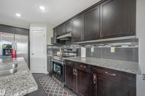 Kitchen featuring dark wood cabinetry, stainless steel appliances, granite countertops, a stainless steel sink, and recessed lighting - 3359 13 Avenue Nw, Edmonton, AB 