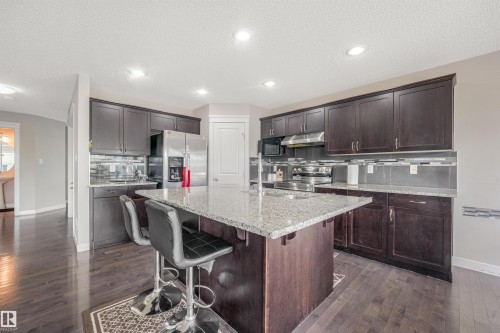 Kitchen featuring wood-finish flooring, dark wood cabinetry, light granite countertops, stainless steel appliances, and recessed lighting - 3359 13 Avenue Nw, Edmonton, AB 
