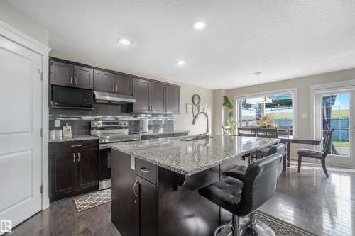 Kitchen featuring dark wood cabinetry, stainless steel appliances, granite countertops, and wood-finish flooring - 3359 13 Avenue Nw, Edmonton, AB 