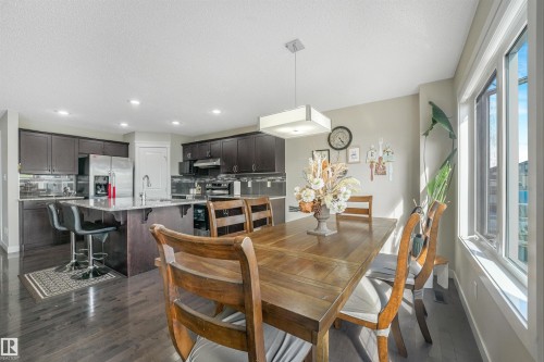 Spacious open-concept living area featuring wood-finish flooring, a kitchen island with seating, dark wood cabinetry, and a large window - 3359 13 Avenue Nw, Edmonton, AB 