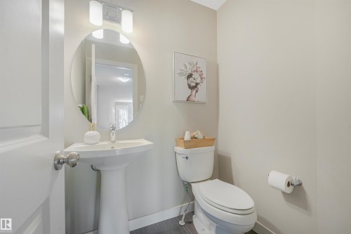 Pedestal sink with a chrome faucet, oval wall mirror, and a two-light vanity fixture - 3359 13 Avenue Nw, Edmonton, AB 