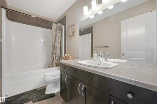 White tub and shower combination with dark tile surround, dark wood-finish vanity with a single basin, and large wall-mounted mirror - 3359 13 Avenue Nw, Edmonton, AB 