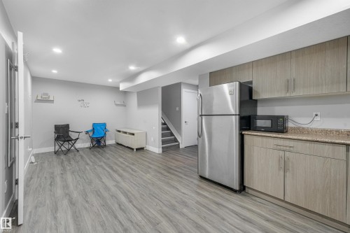 Recessed lighting, wood-finish flooring, light grey walls, light wood-finish cabinetry, and stainless steel refrigerator - 3359 13 Avenue Nw, Edmonton, AB 