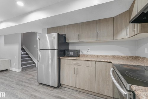Kitchenette featuring wood-finish cabinetry, speckled countertops, and a full-size stainless steel refrigerator - 3359 13 Avenue Nw, Edmonton, AB 