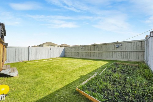 Expansive backyard featuring a manicured lawn, a raised garden bed, and wood privacy fencing with integrated lighting - 3359 13 Avenue Nw, Edmonton, AB 