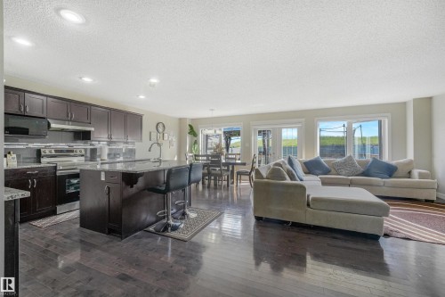 Open-concept living space with dark wood-finish flooring, recessed lighting, and a kitchen island with seating - 3359 13 Avenue Nw, Edmonton, AB 