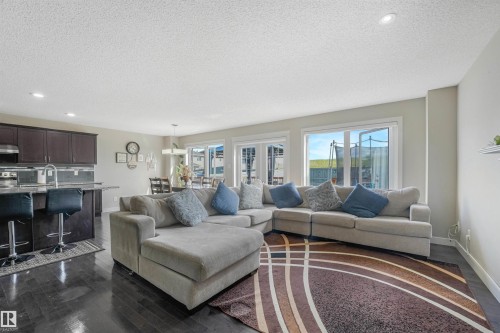 Open-concept living area featuring dark wood-finish flooring, a kitchen island with built-in seating, dark wood cabinetry, and multiple large windows - 3359 13 Avenue Nw, Edmonton, AB 