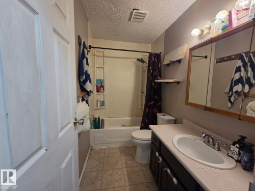 Bathroom featuring a built-in tub with shower, vanity with integrated sink, wood-finish medicine cabinet, and tiled flooring - 3511 28 Avenue Nw, Edmonton, AB - Indoor Photo Showing Bathroom