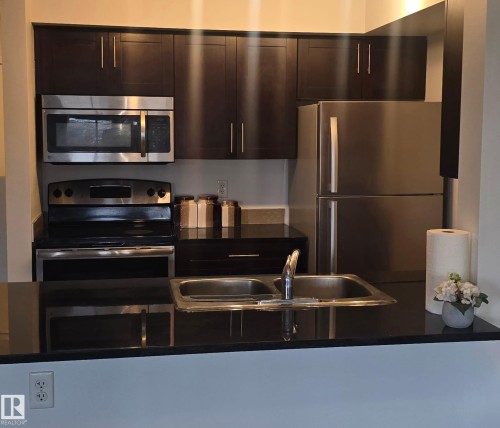 Kitchen featuring dark wood-finish cabinetry, stainless steel appliances, dark countertops, and a double basin sink - #118 1510 Watt Dr Sw, Edmonton, AB - Indoor Photo Showing Kitchen With Stainless Steel Kitchen With Double Sink With Upgraded Kitchen