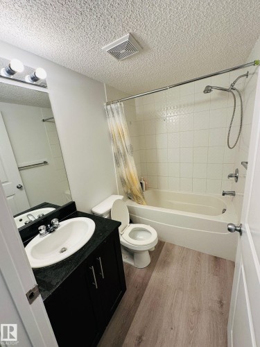 Bathroom featuring a dark wood-finish vanity, light-toned flooring, white tiled shower surround, and a full-size bathtub - #118 1510 Watt Dr Sw, Edmonton, AB - Indoor Photo Showing Bathroom