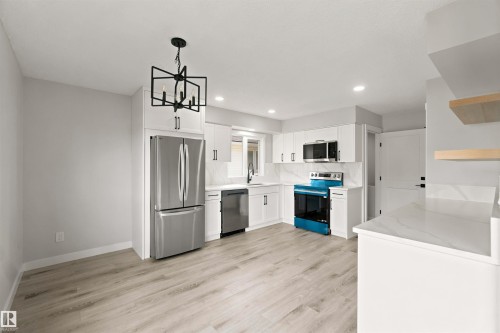 Kitchen featuring light wood-finish flooring, white cabinetry, integrated stainless steel appliances, a geometric chandelier, and recessed lighting - 4129 134A Avenue Nw, Edmonton, AB - Indoor Photo Showing Kitchen