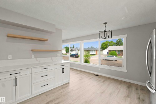 White shaker-style cabinetry with black hardware, wood-finish flooring, a contemporary chandelier, two floating wood shelves, and large windows - 4129 134A Avenue Nw, Edmonton, AB - Indoor