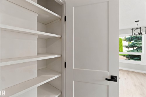 Built-in shelving, contrasting matte black hardware, white interior door, light wood-finish flooring, and a modern ceiling fixture - 4129 134A Avenue Nw, Edmonton, AB - Indoor With Storage