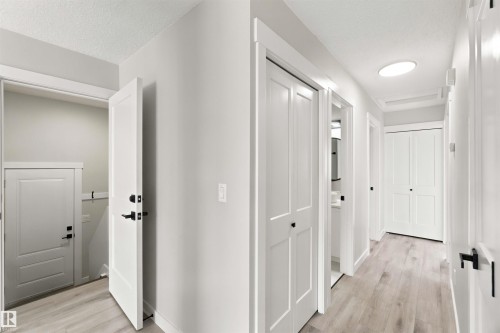 Light-toned wood-finish flooring throughout, white interior doors with matte black hardware, recessed ceiling lighting, and crisp white trimwork - 4129 134A Avenue Nw, Edmonton, AB - Indoor Photo Showing Other Room