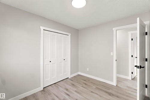 Wood-finish flooring, bi-fold closet doors with black hardware, white trim, and a ceiling-mounted light fixture - 4129 134A Avenue Nw, Edmonton, AB - Indoor Photo Showing Other Room