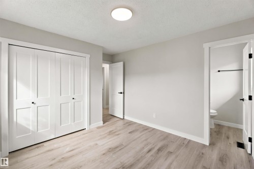 Light-toned wood-finish flooring, white bifold closet doors with black hardware, white trim, and a flush-mount ceiling light - 4129 134A Avenue Nw, Edmonton, AB - Indoor Photo Showing Other Room