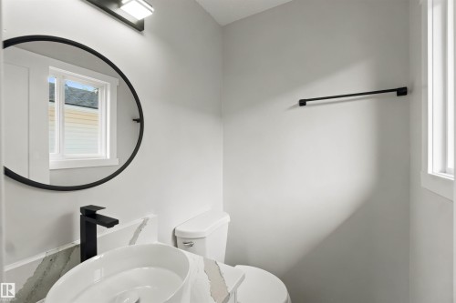 Black framed circular mirror, white oval vessel sink, matte black faucet, and a black towel bar - 4129 134A Avenue Nw, Edmonton, AB - Indoor Photo Showing Bathroom