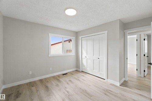 Light wood-finish flooring, white trim, and a white bi-fold closet door - 4129 134A Avenue Nw, Edmonton, AB - Indoor Photo Showing Other Room