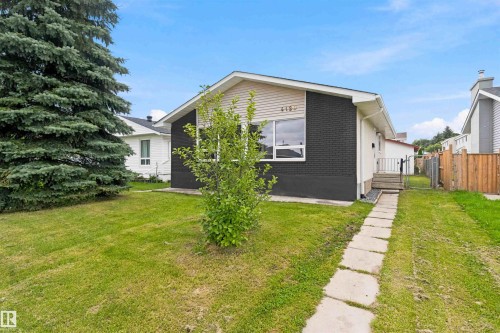 Well-maintained exterior with dark brick and light siding, featuring a front yard with mature landscaping, a concrete-paver pathway, and an established evergreen tree - 4129 134A Avenue Nw, Edmonton, AB - Outdoor