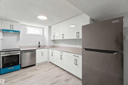 Kitchen featuring white cabinetry, light-toned countertops, stainless steel appliances, and wood-finish flooring - 4129 134A Avenue Nw, Edmonton, AB - Indoor Photo Showing Kitchen