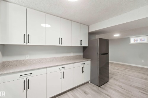 White cabinetry with modern black hardware, light-toned countertops, and wood-finish flooring - 4129 134A Avenue Nw, Edmonton, AB - Indoor