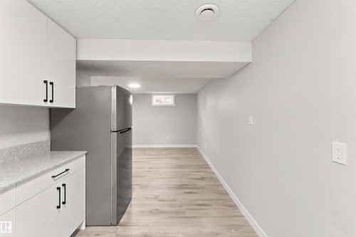White cabinetry with black hardware, stone-finish countertop, stainless steel refrigerator, recessed lighting, and wood-finish flooring - 4129 134A Avenue Nw, Edmonton, AB - Indoor