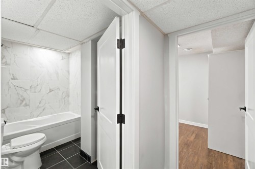Bathroom featuring a built-in bathtub, toilet, and marble-patterned wall tiling - 4129 134A Avenue Nw, Edmonton, AB - Indoor Photo Showing Bathroom