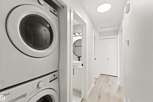 Stackable washer and dryer, wood-finish flooring, white solid-core doors, recessed ceiling light, and skylight - 4129 134A Avenue Nw, Edmonton, AB - Indoor Photo Showing Laundry Room