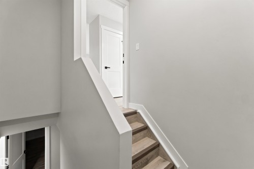 Staircase featuring wood-finish treads and white risers, framed by a white railing and neutral wall tones - 4129 134A Avenue Nw, Edmonton, AB - Indoor Photo Showing Other Room