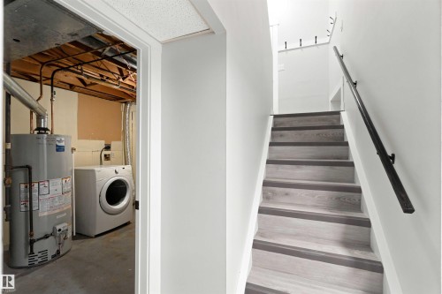 Wood-finish staircase with dark treads and a black metal handrail - 4129 134A Avenue Nw, Edmonton, AB - Indoor Photo Showing Laundry Room