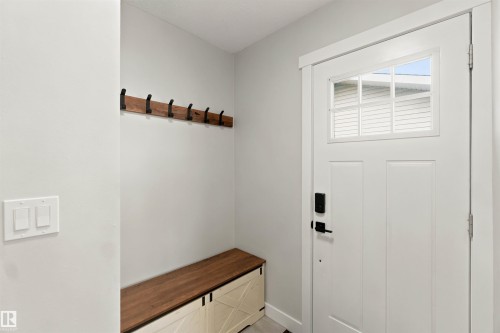 Entryway featuring a paneled door with integrated window, a wood-finish bench with decorative doors, a wood-finish coat rack with dark metal hooks, and light-toned wall finishes - 4129 134A Avenue Nw, Edmonton, AB - Indoor Photo Showing Other Room