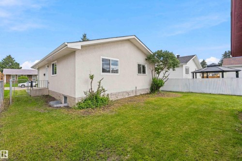 Expansive green lawn with a white lattice fence, featuring a white stucco exterior and white trim windows - 4129 134A Avenue Nw, Edmonton, AB - Outdoor With Exterior