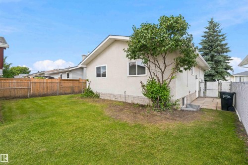 Expansive rear yard featuring a manicured lawn, wood fencing, concrete patio, and stucco exterior - 4129 134A Avenue Nw, Edmonton, AB - Outdoor