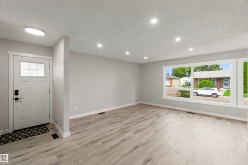 Light wood-finish flooring, recessed lighting, expansive front-facing window, white trim, and a white entry door with frosted glass panes - 4129 134A Avenue Nw, Edmonton, AB - Indoor Photo Showing Other Room