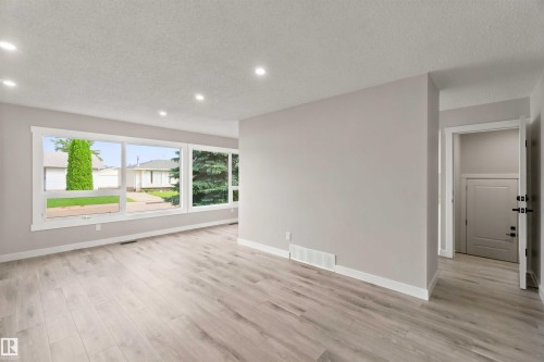 Spacious open-concept room featuring light wood-finish flooring, recessed ceiling lighting, and expansive windows - 4129 134A Avenue Nw, Edmonton, AB - Indoor