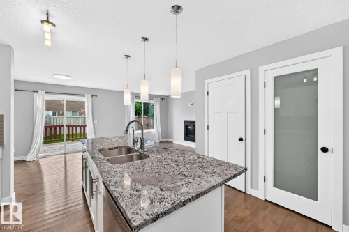 Kitchen island with dual stainless steel sink and stone countertop, wood-finish flooring, and white paneled doors - 1112 176 Street Sw, Edmonton, AB - Indoor Photo Showing Kitchen With Double Sink With Upgraded Kitchen