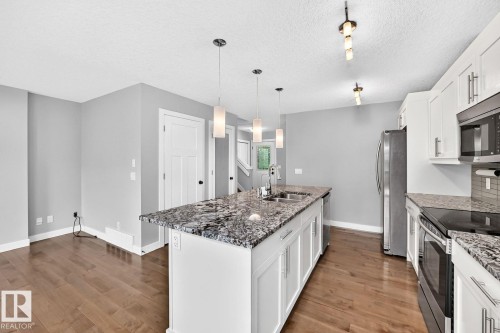 Kitchen featuring a large central island with a double sink, pendant lighting, white cabinetry, and granite countertops - 1112 176 Street Sw, Edmonton, AB - Indoor Photo Showing Kitchen With Double Sink With Upgraded Kitchen