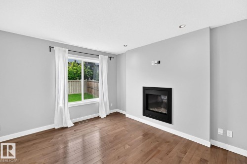 Wood-finish flooring throughout, recessed lighting, built-in fireplace, and a large window - 1112 176 Street Sw, Edmonton, AB - Indoor Photo Showing Living Room With Fireplace