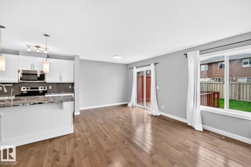 Open-concept living space featuring wood-finish flooring, white cabinetry, stainless steel appliances, and a tiled backsplash - 1112 176 Street Sw, Edmonton, AB - Indoor Photo Showing Kitchen With Double Sink