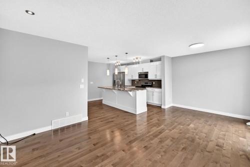 Hardwood-finish flooring throughout, bright recessed lighting, white cabinetry, integrated stainless steel appliances, and a kitchen island with stone countertops - 1112 176 Street Sw, Edmonton, AB - Indoor Photo Showing Kitchen