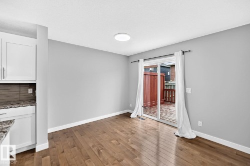 Wood-finish flooring, white cabinetry with silver-tone hardware, a sliding glass door, and a built-in deck with privacy fencing - 1112 176 Street Sw, Edmonton, AB - Indoor Photo Showing Other Room