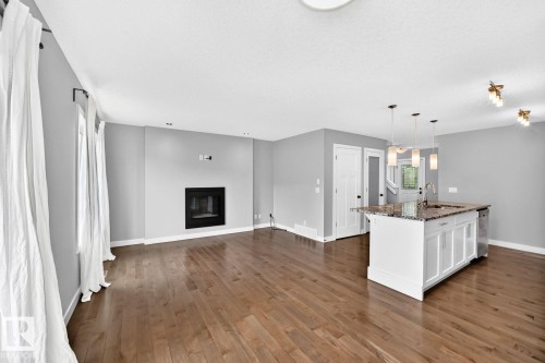 Hardwood flooring, fireplace, kitchen island with pendant lighting, white cabinetry, and stainless steel dishwasher - 1112 176 Street Sw, Edmonton, AB - Indoor With Fireplace