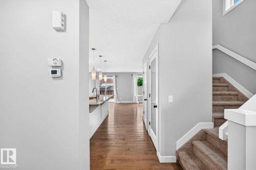 Hardwood flooring extending into the main living area, a carpeted staircase with white risers, and a kitchen island with pendant lighting - 1112 176 Street Sw, Edmonton, AB - Indoor Photo Showing Other Room