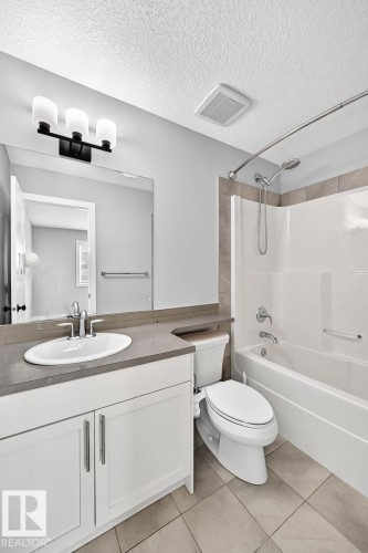 Bathroom featuring a white vanity with a single basin sink, a gray countertop, an integrated toilet, and a bathtub with a shower and tiled surround - 1112 176 Street Sw, Edmonton, AB - Indoor Photo Showing Bathroom