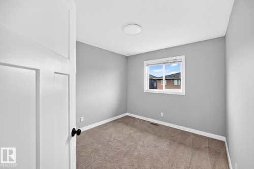 Neutral gray wall paint, textured carpet, white window frame, and a flush-mount ceiling light - 1112 176 Street Sw, Edmonton, AB - Indoor Photo Showing Other Room